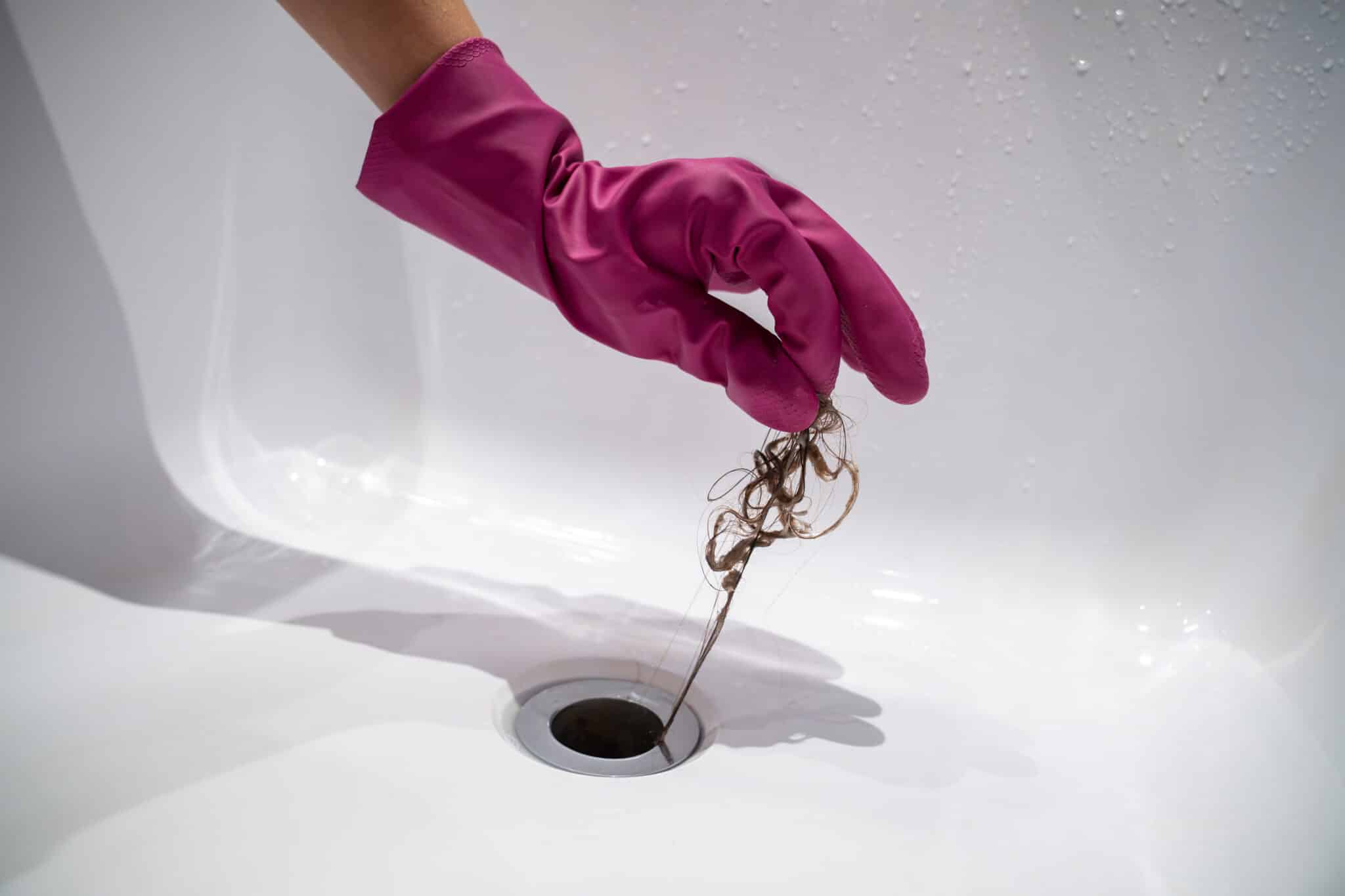 Hand of woman in pink rubber glove taking off hair clump from water drain, blocked pipe in bath., Bathroom Drain.