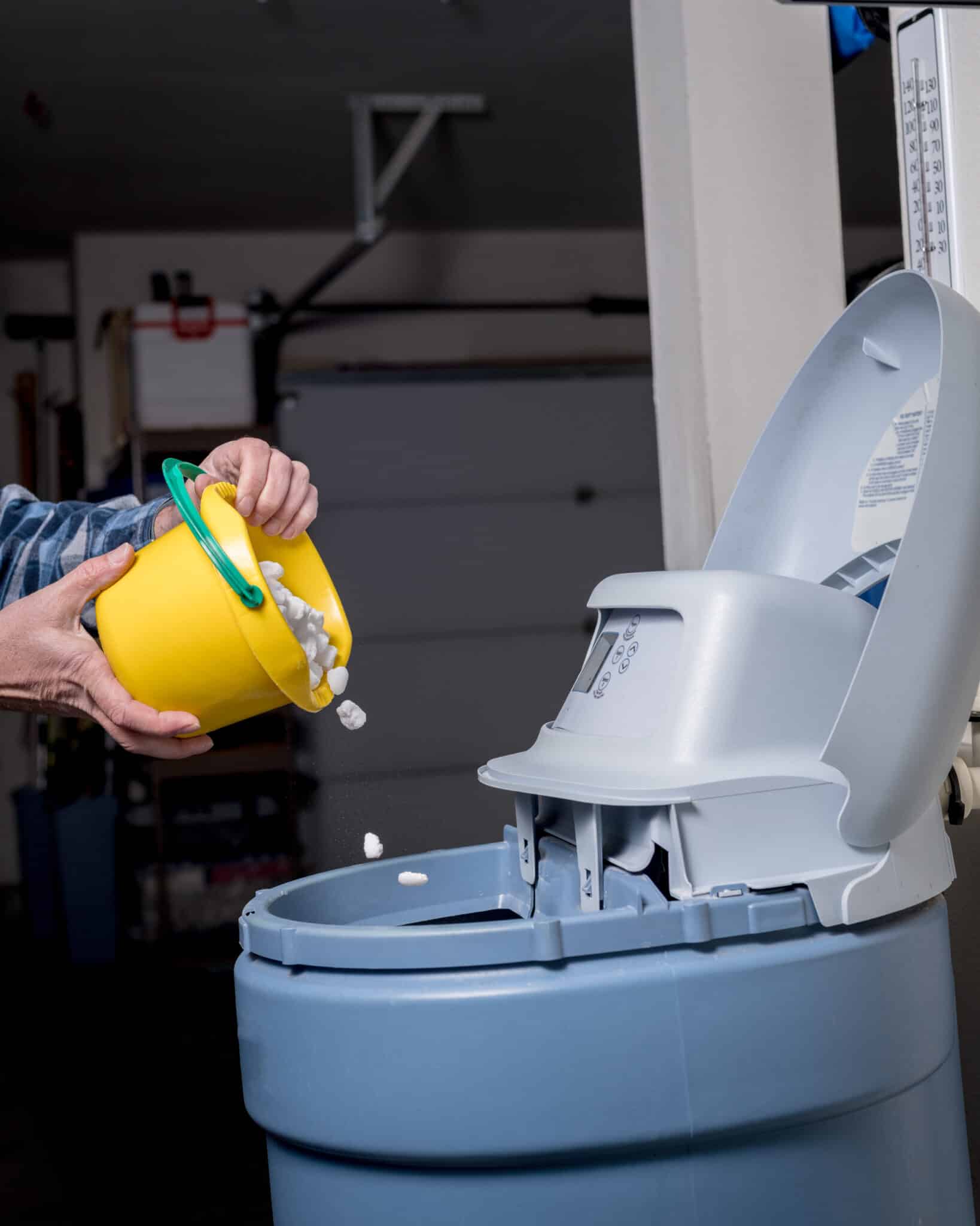 Salt pellets are poured form a yellow bucket into a blue water softener, Plumbing Scale Buildup.