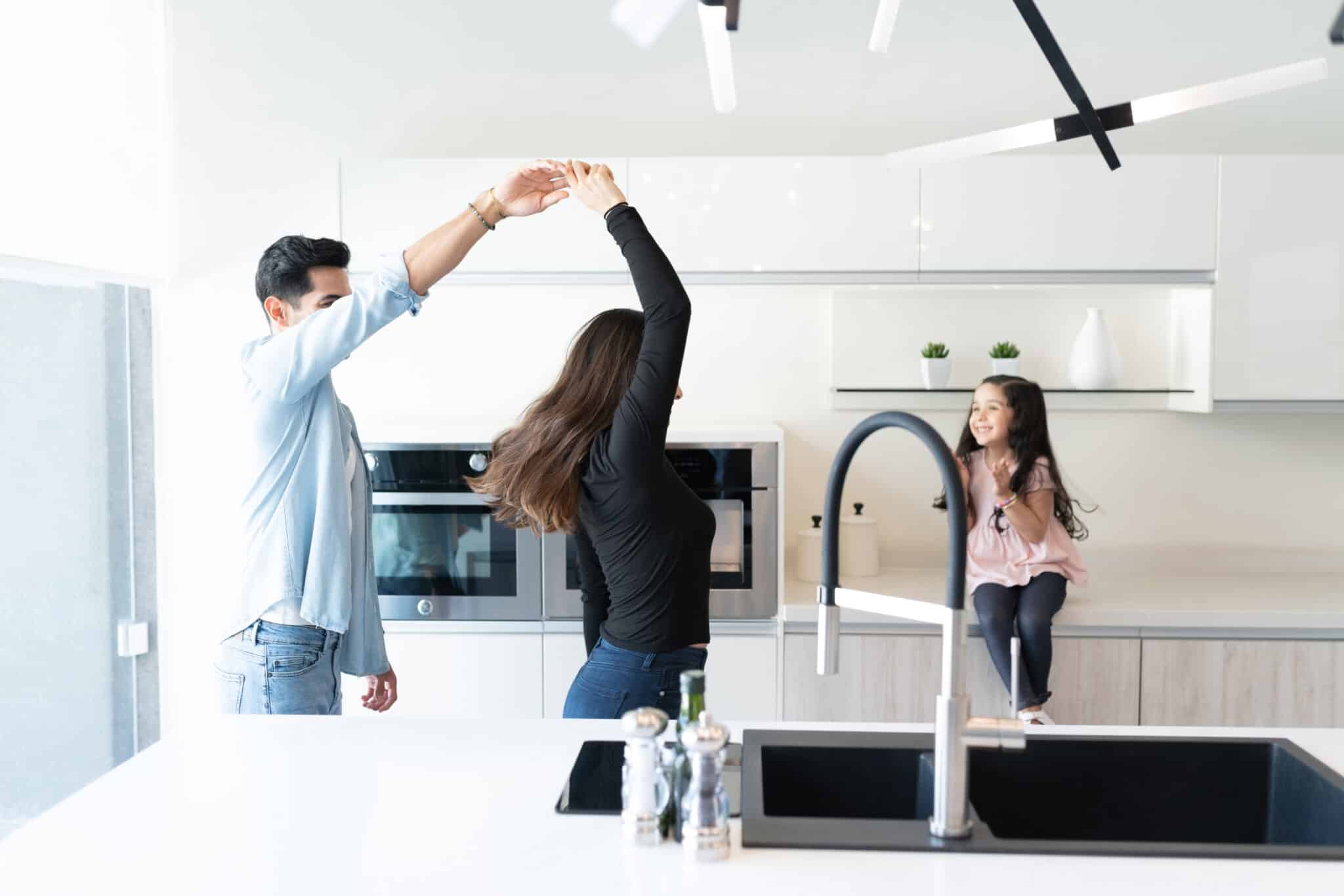 Parents dancing while smiling daughter sitting on kitchen counter, Water Leak Sensor.