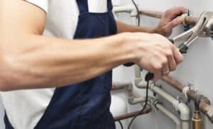 Professional plumber repairing pipes with a pipe wrench to ensure clean pipes and a clean home.