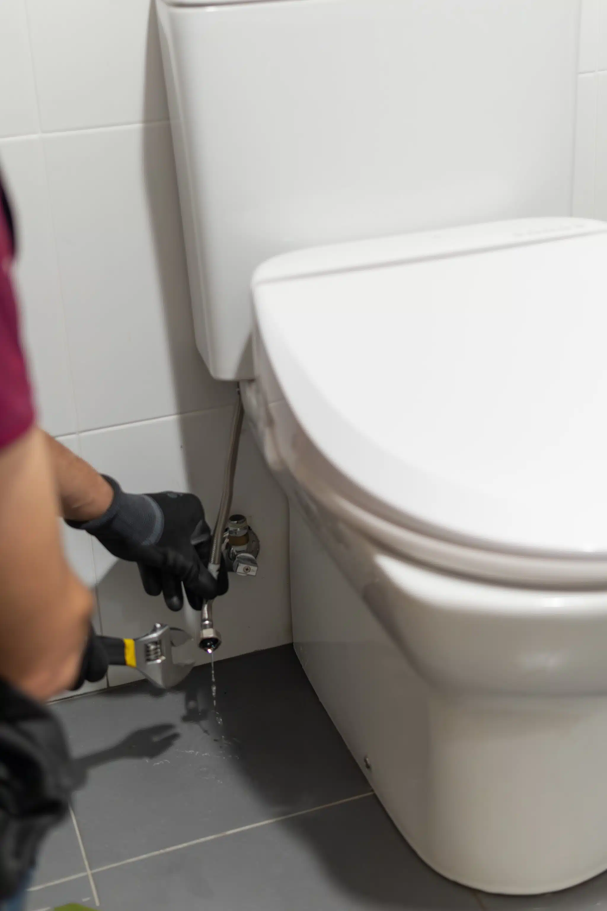 Wrench fixes a water leak from a white toilet, Toilet supply line leak.
